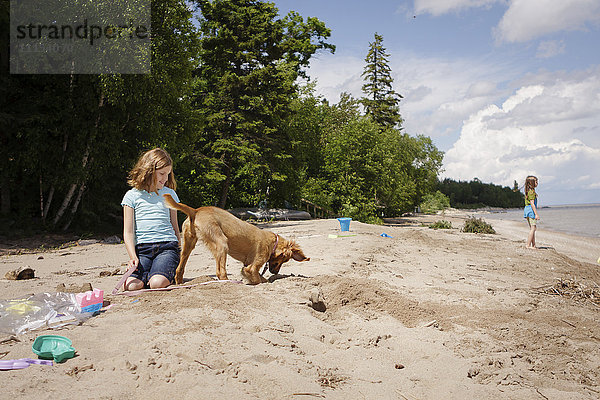 Kaukasisches Mädchen und Welpe spielen am Strand