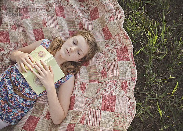 Kaukasisches Mädchen schlafend mit Buch auf Decke