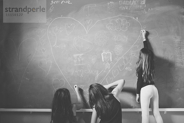 Kaukasische Mädchen  die auf einer Kreidetafel im Klassenzimmer zeichnen