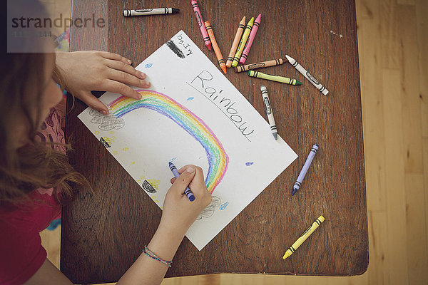 Kaukasisches Mädchen zeichnet Regenbogen mit Buntstiften auf Tisch