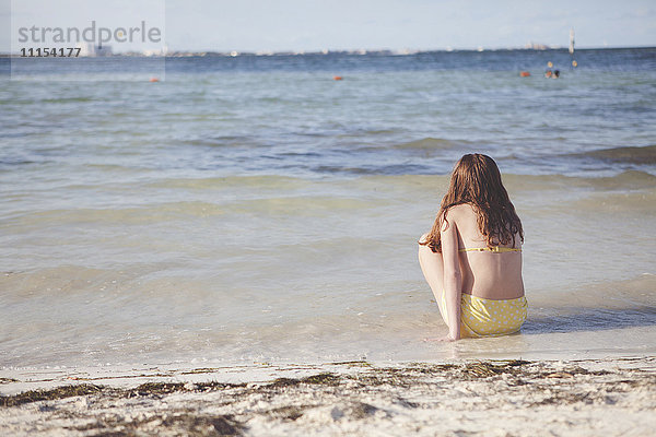 Kaukasisches Teenager-Mädchen sitzt in den Wellen am Strand