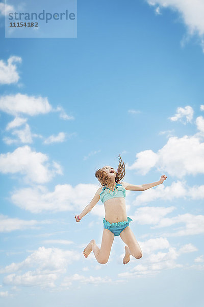 Kaukasisches Mädchen springt vor Freude in den blauen Himmel