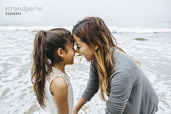 Hispanische Mutter und Tochter stehen am Strand