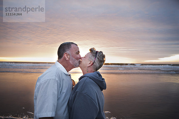 Kaukasisches Paar  das sich bei Sonnenuntergang am Strand küsst