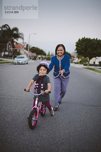 Großmutter bringt ihrer Enkelin auf einer Vorstadtstraße das Fahrradfahren bei
