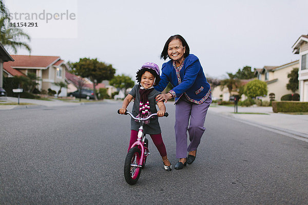 Großmutter bringt ihrer Enkelin auf einer Vorstadtstraße das Fahrradfahren bei