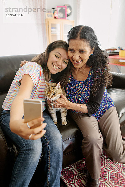 Großmutter und Enkelin machen Selfie mit Katze auf Sofa
