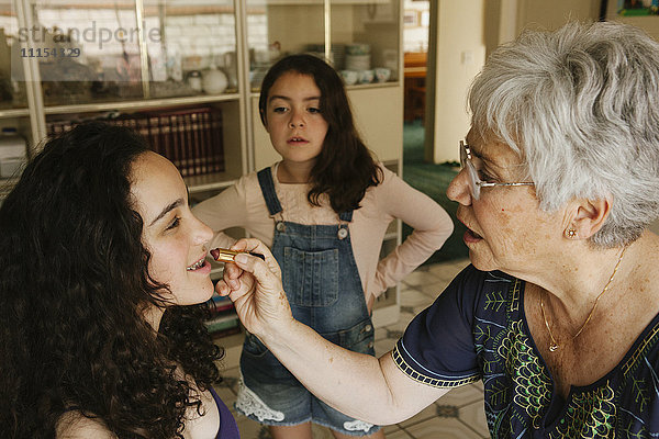 Großmutter trägt Lippenstift auf Enkelin im Esszimmer auf