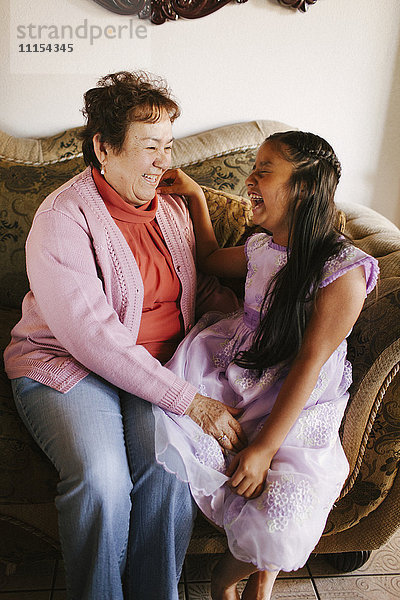 Hispanische Großmutter und Enkelin lachend auf dem Sofa