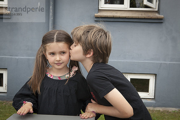 Kaukasischer Junge küsst Schwester im Hinterhof