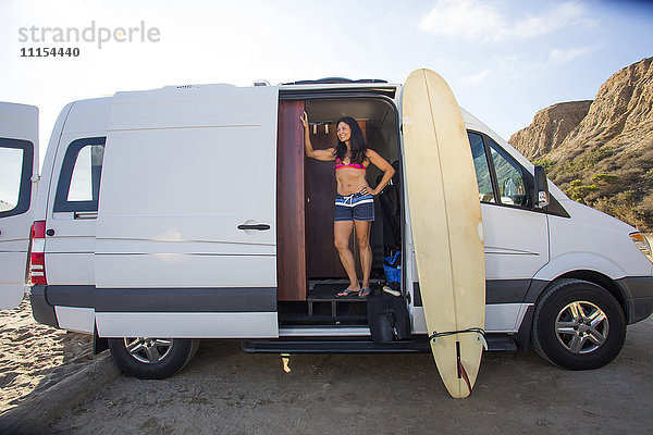 Hispanischer Surfer mit Surfbrett im Van stehend