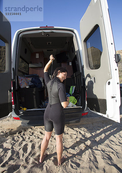 Hispanischer Surfer  der seinen Neoprenanzug am Strand zuzieht