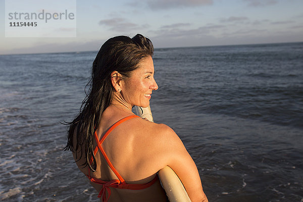 Hispanische Frau hält Surfbrett im Meer