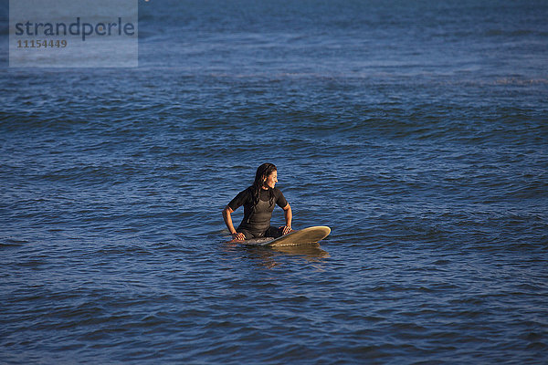 Hispanischer Surfer schwimmt auf Surfbrett im Meer
