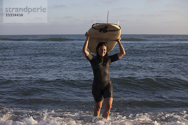 Hispanischer Surfer mit Surfbrett im Meer
