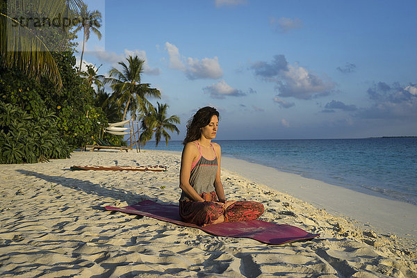 Kaukasische Frau meditiert am tropischen Strand