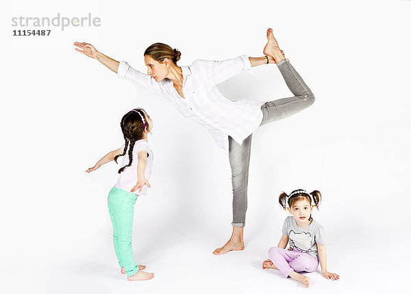 Mutter übt Yoga mit verspielten Töchtern