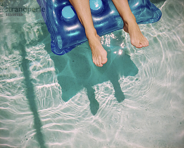 Füße einer kaukasischen Frau schwimmen auf einem Floß im Schwimmbad