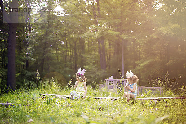 Mädchen spielen Telefon auf einem Holzklotz im Garten