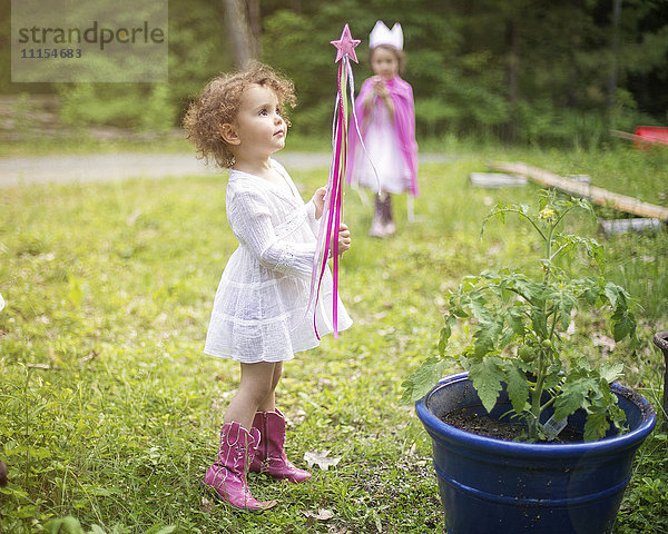Mädchen spielt mit Zauberstab im Hinterhof Garten