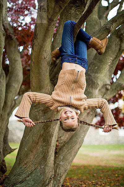 Lächelndes Mädchen hängt kopfüber in einem Baum