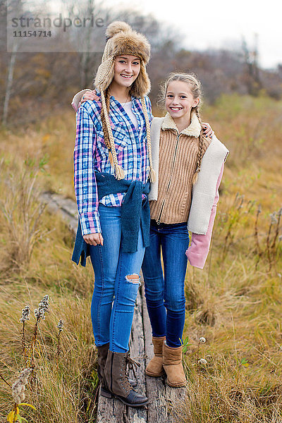 Lächelnde Schwestern auf einem Holzsteg in einem Feld
