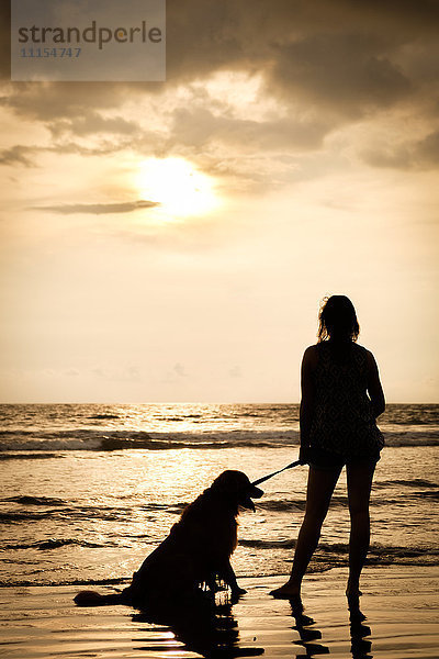 Mexiko  Nayarit  Silhouette einer jungen Frau mit ihrem Hund an der Leine am Strand bei Sonnenuntergang