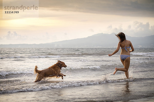 Mexiko  Nayarit  Junge Frau im Bikini beim Spielen mit ihrem Golden Retriever Hund am Strand