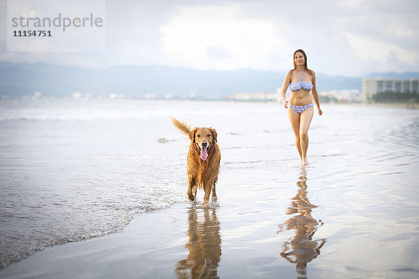 Mexiko  Nayarit  Junge Frau  die mit ihrem Golden Retriever Hund am Strand spazieren geht.