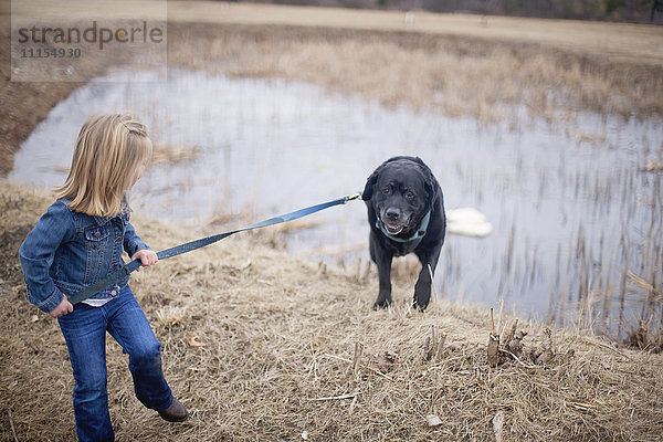 Mädchen zieht Hund an der Leine in der Nähe eines ländlichen Teichs