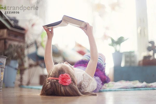 Mädchen liest ein Buch auf dem Boden im Wohnzimmer