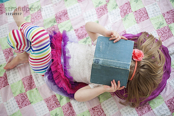 Mädchen liest Buch auf Decke