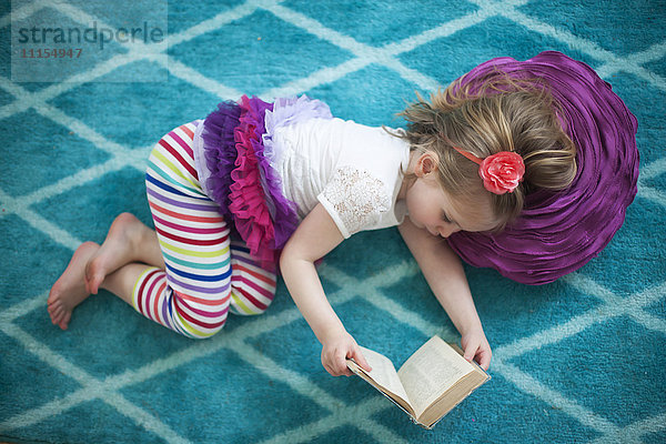 Mädchen liest Buch auf dem Boden