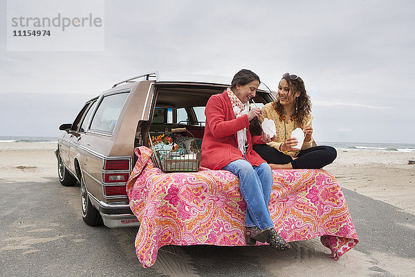 Kaukasische Mutter und Tochter beim Picknick im Kofferraum eines Autos am Strand