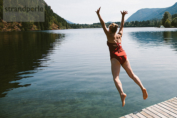 Kaukasische Frau springt vom Steg in einen ländlichen See