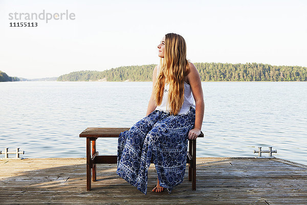 Kaukasisches Teenager-Mädchen sitzt auf einem Holzsteg am See