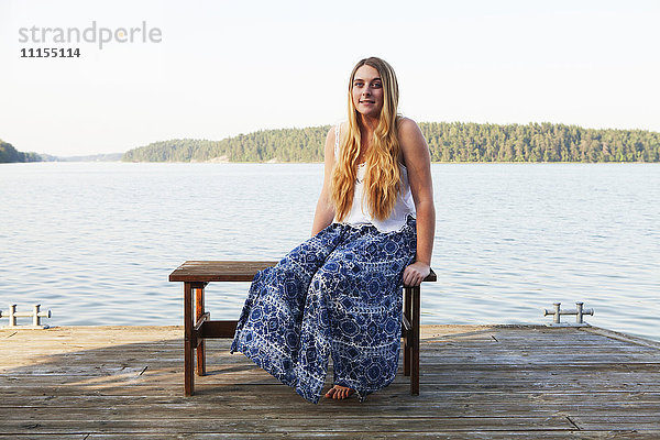 Kaukasisches Teenager-Mädchen sitzt auf einem Holzsteg am See