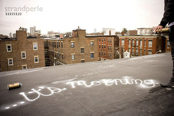Graffitikünstler sprüht Farbe auf ein städtisches Hausdach