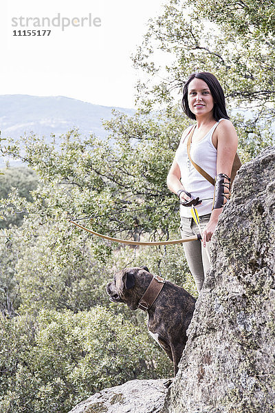 Porträt der lächelnden Bogenschützin mit ihrem Hund in der Natur