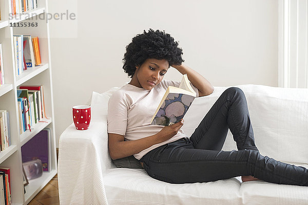 Schwarze Frau liest Buch auf Sofa