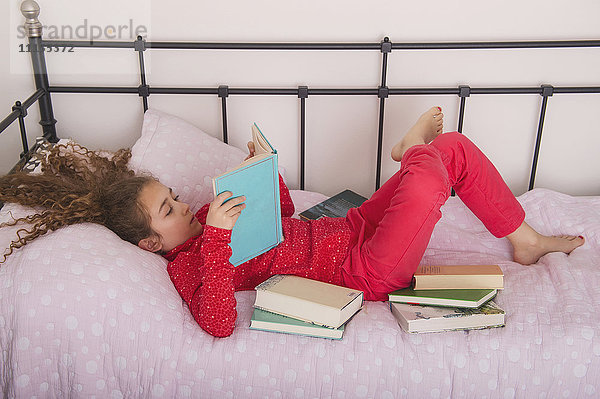 Kaukasisches Mädchen liest Bücher auf dem Bett