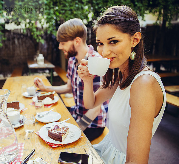 Lächelnde junge Frau mit Freund im Freien bei Kaffee und Kuchen