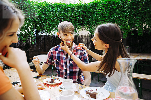 Glückliches junges Paar mit Freund im Freien bei Kaffee und Kuchen