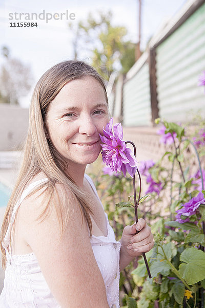 Gemischtrassige Frau riecht an Blumen im Garten