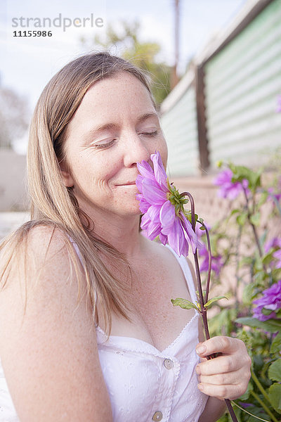 Gemischtrassige Frau riecht an Blumen im Garten