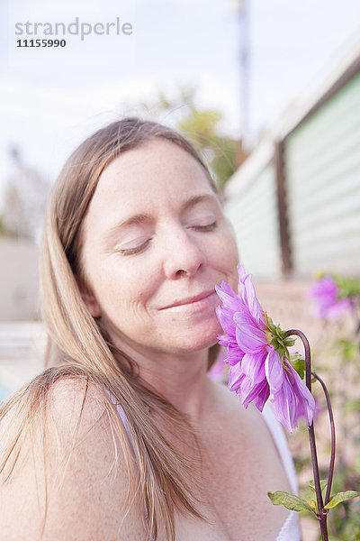 Gemischtrassige Frau riecht an Blumen im Garten