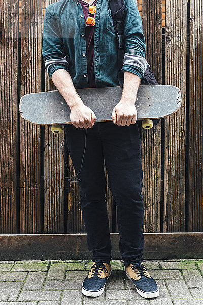 Junger Mann auf dem Bürgersteig stehend mit Skateboard  Teilansicht