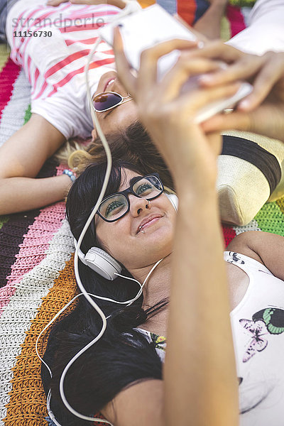 Junge Frau mit Freunden  die auf der Decke liegen und Musik hören.