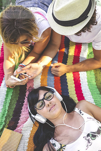 Junge Frau mit Freunden  die auf der Decke liegen und Musik hören.