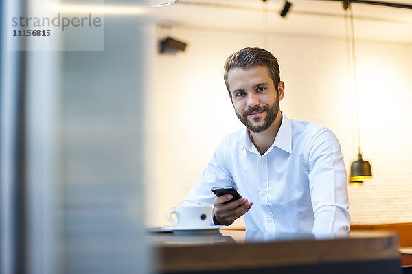 Porträt eines lächelnden Geschäftsmannes mit Handy im Cafe
